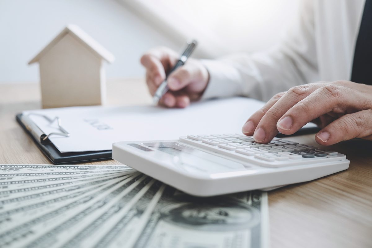 Calcul des frais d’acquisition : calculatrice, billets et maquette de maison sur un bureau